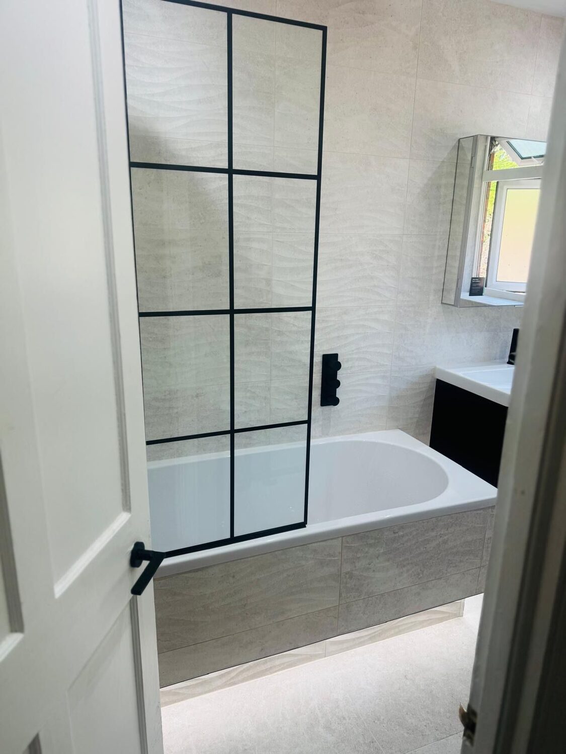 Bathroom with black-framed crittall-style bath screen and textured wall tiles