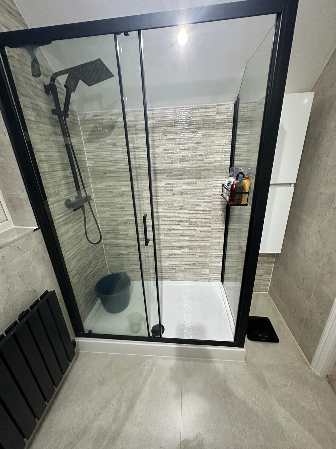 Black-framed sliding shower enclosure with stone-effect tiles